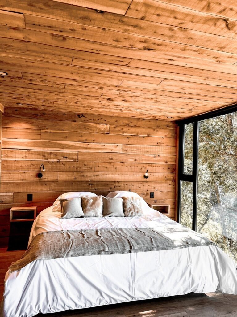 Bedroom with a king-size bed, wooden walls and a window onto the forest